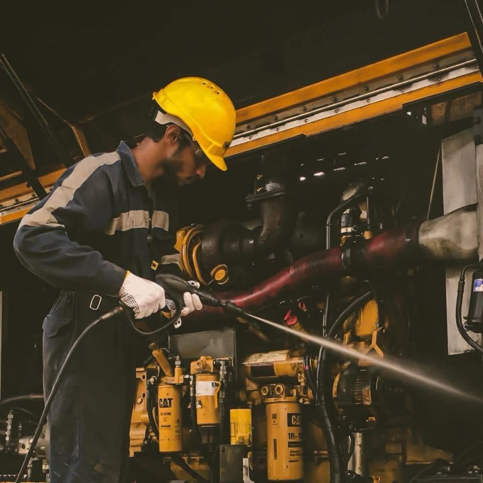 Jani servicing a diesel engine in workshop overalls and a hard hat